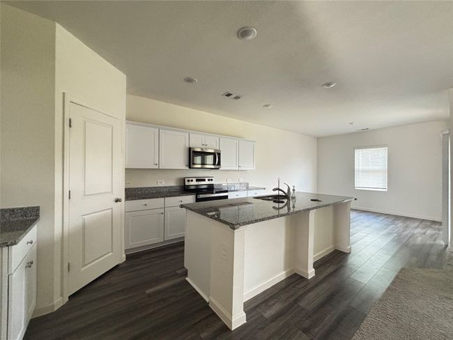 Kitchen featuring dark wood finished floors, appliances with stainless steel finishes, white cabinetry, dark stone counters, and a center island with sink | Image 8