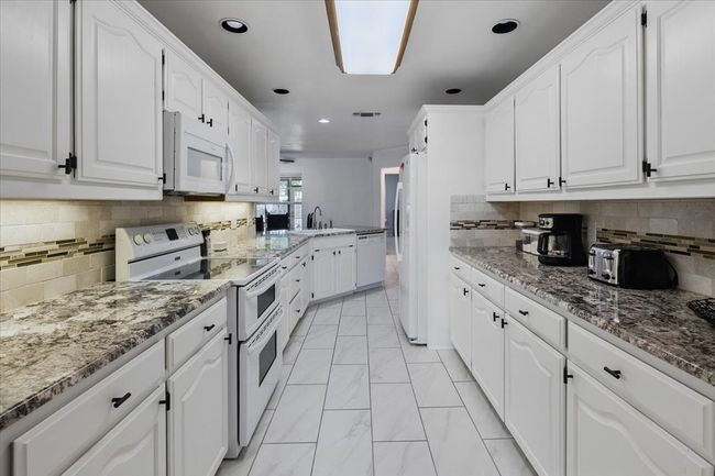 Kitchen with white appliances, light marble finish flooring, white cabinetry, a sink, and recessed lighting | Image 13