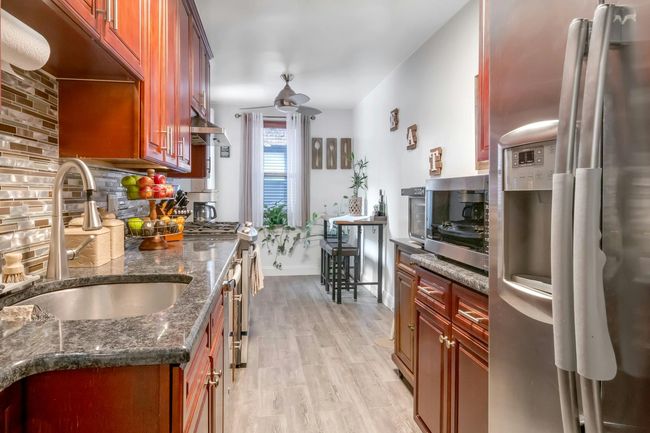 Kitchen with stainless steel appliances, tasteful backsplash, light wood-style floors, dark stone countertops, and brown cabinetry | Image 9