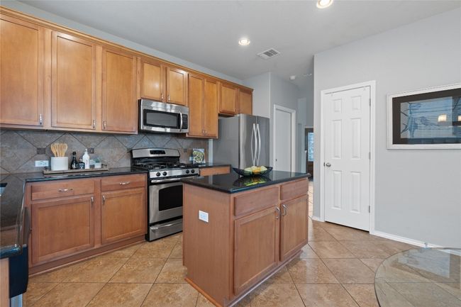 Kitchen with appliances with stainless steel finishes, decorative backsplash, a center island, light tile patterned floors, and brown cabinets | Image 16