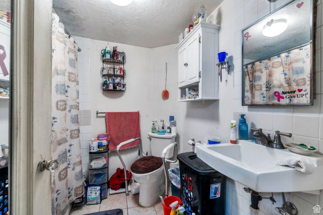 Full bath with toilet, tile patterned floors, a textured ceiling, a sink, and a shower with curtain | Image 8
