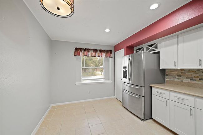 Bright kitchen space with modern stainless steel appliances, white cabinetry, and a stone backsplash. It features a window with a view outside, recessed lighting, and a charming light fixture. Space is large enough for breakfast/ small dinning area. | Image 15