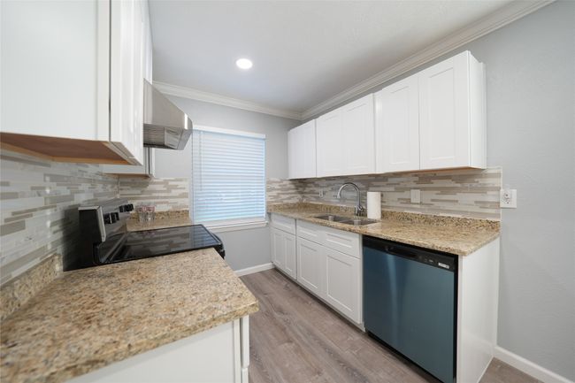 Kitchen with ornamental molding, a sink, stainless steel electric stove, wall chimney exhaust hood, and dishwashing machine | Image 5