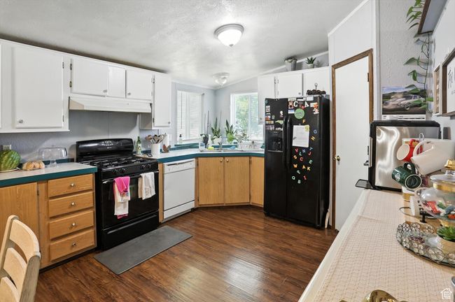 Kitchen featuring black appliances, under cabinet range hood, dark wood finished floors, light countertops, and vaulted ceiling | Image 7
