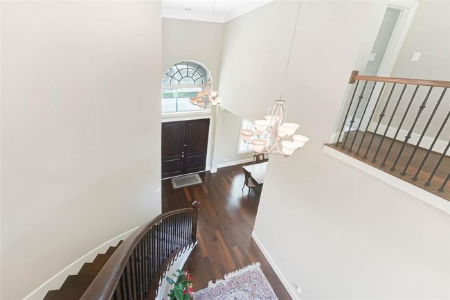 Dramatic two-story foyer with sweeping staircase, double entry doors, and an arched transom window that fills the space with natural light. Elegant iron balusters and chandelier add a touch of sophistication. | Image 7