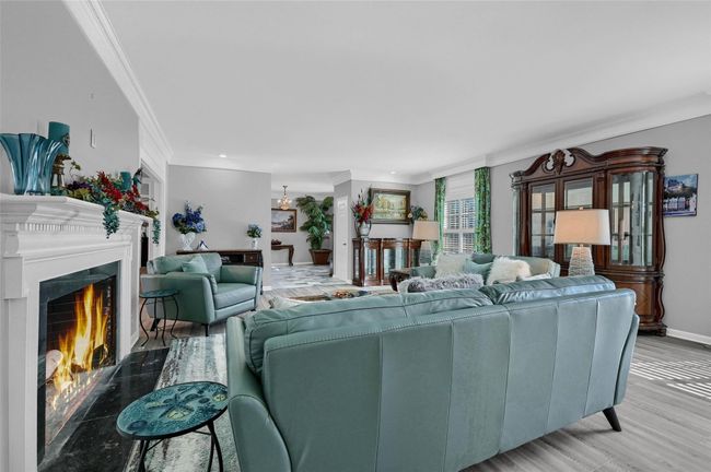 Living area featuring crown molding, a warm lit fireplace, baseboards, and light wood-style floors | Image 11
