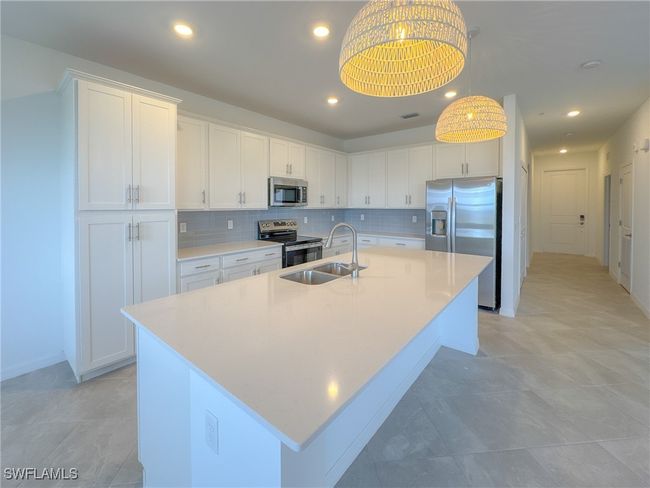 Kitchen featuring stainless steel appliances, a sink, an island with sink, white cabinetry, and light countertops | Image 8