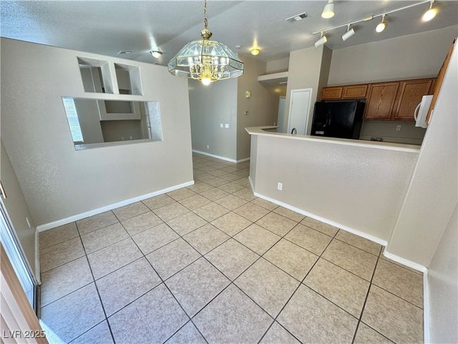 Kitchen with light tile patterned flooring, visible vents, freestanding refrigerator, a notable chandelier, and brown cabinets | Image 9