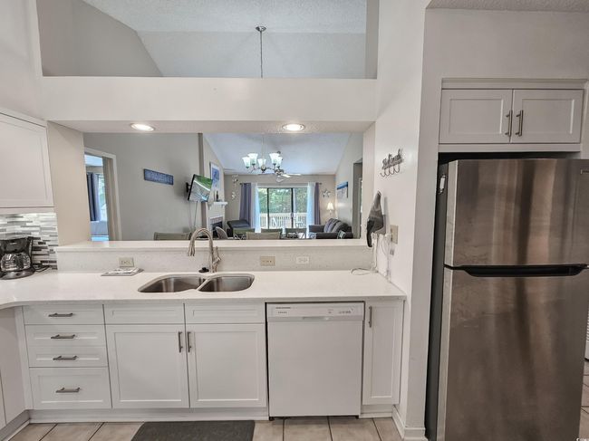 Kitchen with freestanding refrigerator, dishwasher, a sink, a chandelier, and light tile patterned floors | Image 15