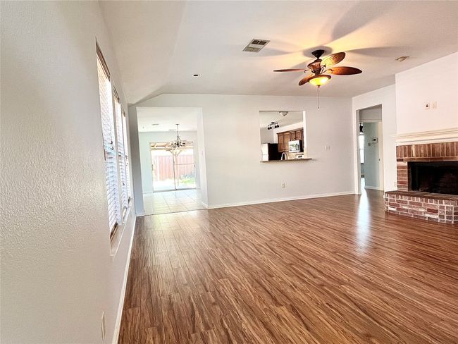 Unfurnished living room with wood finished floors, ceiling fan, a fireplace, vaulted ceiling, and a chandelier | Image 12