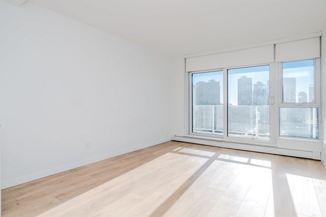 Empty room featuring a baseboard radiator, light wood finished floors, baseboards, and a view of city | Image 11