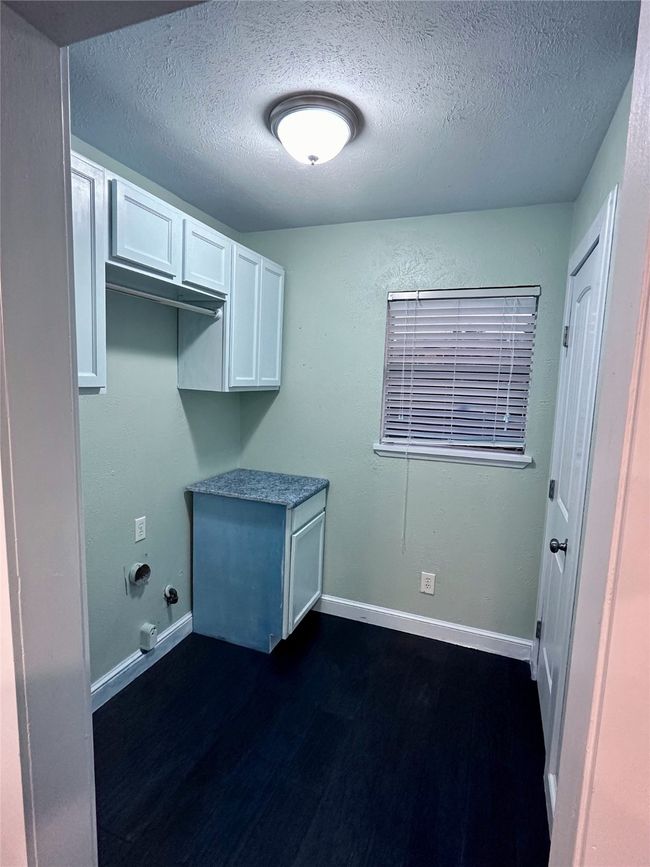 Laundry area featuring a textured ceiling, dark wood-type flooring, and cabinet space | Image 15