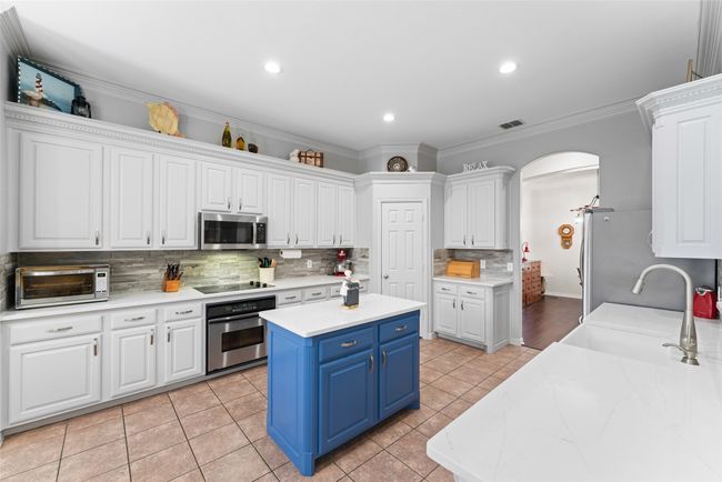 Kitchen featuring appliances with stainless steel finishes, blue cabinetry, white cabinets, arched walkways, and crown molding | Image 9