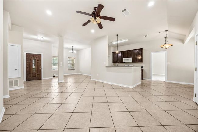 Unfurnished living room with ceiling fan with notable chandelier, light tile patterned floors, and visible vents | Image 9