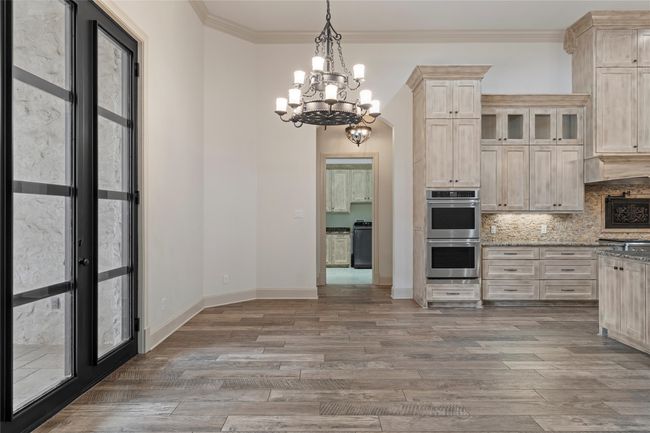 Kitchen with stainless steel double oven, tasteful backsplash, light wood-type flooring, light stone counters, and a notable chandelier | Image 10