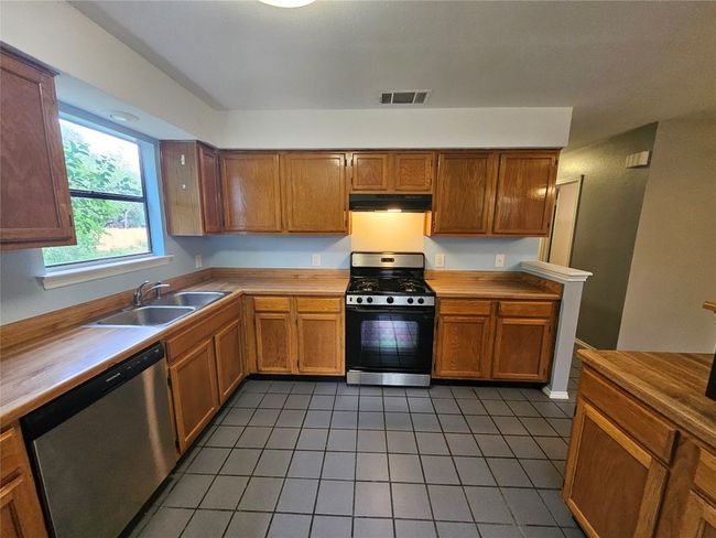 Kitchen featuring a sink, tile patterned floors, visible vents, under cabinet range hood, and appliances with stainless steel finishes | Image 16