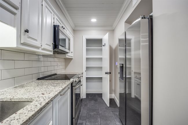 Kitchen with new appliances with stainless steel finishes, ornamental molding, white cabinetry, decorative backsplash, and light stone countertops | Image 5