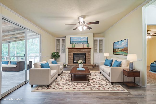 Living room with a ceiling fan, lofted ceiling, wood finished floors, ornamental molding, and a brick fireplace | Image 8