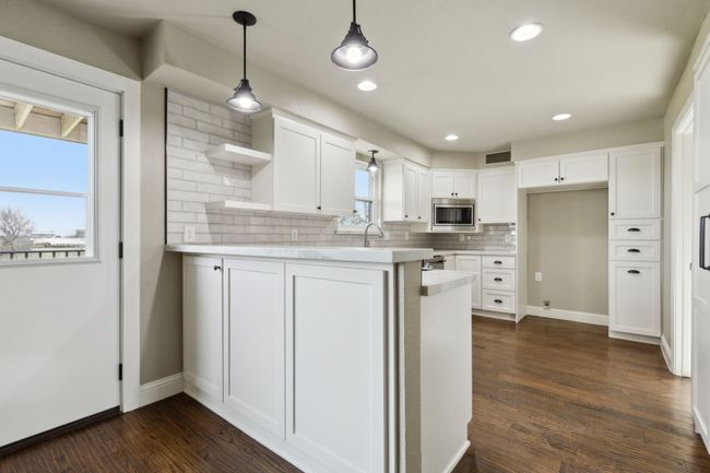 Kitchen with open shelves, stainless steel microwave, white cabinetry, a peninsula, and dark wood-style flooring | Image 11