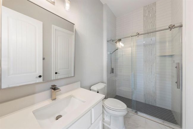 Crisp and contemporary, the en-suite bath features a sleek quartz vanity, frameless glass shower with designer tile inlay, and polished chrome fixtures for a fresh, hotel-inspired finish. | Image 27