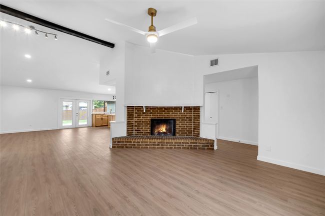 Unfurnished living room featuring ceiling fan, a brick fireplace, wood finished floors, baseboards, and high vaulted ceiling | Image 8
