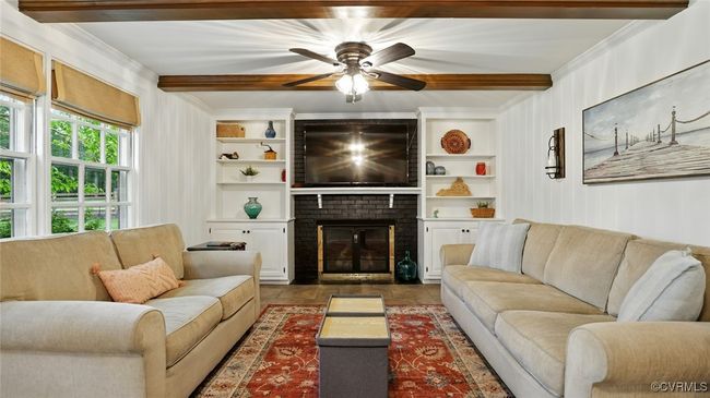 Living room featuring beamed ceiling, a ceiling fan, a brick fireplace, and ornamental molding | Image 35