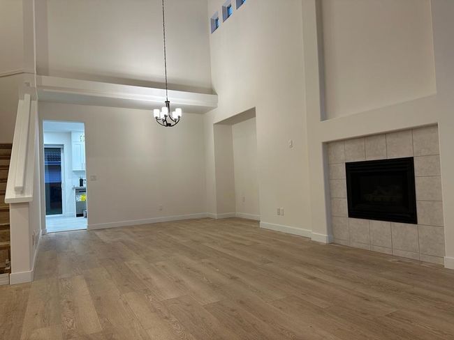 Unfurnished living room with baseboards, light wood-type flooring, a chandelier, and a towering ceiling | Image 4