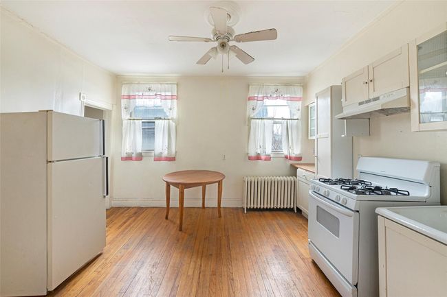 Kitchen with light wood finished floors, radiator, a ceiling fan, white appliances, and under cabinet range hood | Image 10