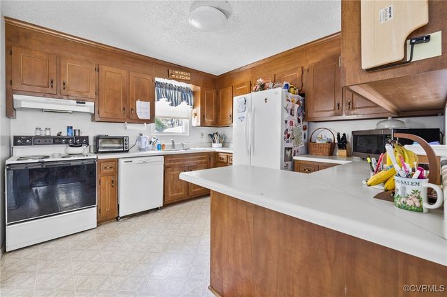 Kitchen featuring a peninsula, white appliances, brown cabinets, light countertops, and under cabinet range hood | Image 22