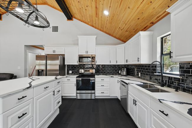 Kitchen featuring stainless steel appliances, visible vents, backsplash, wood ceiling, and a sink | Image 18
