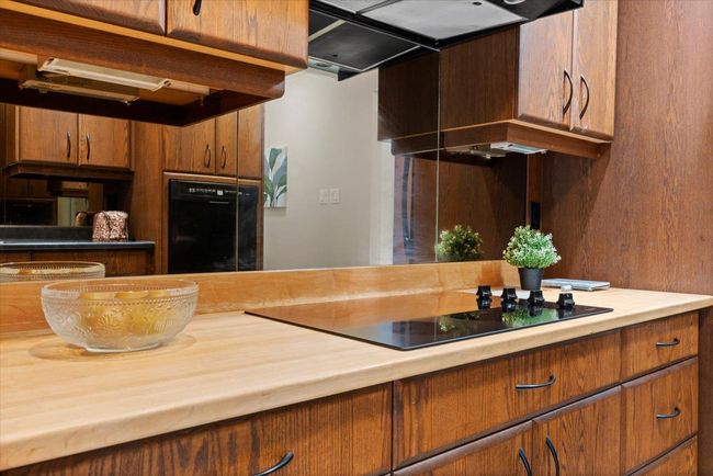 Kitchen featuring black electric stovetop, ventilation hood, brown cabinets, and wall oven | Image 28