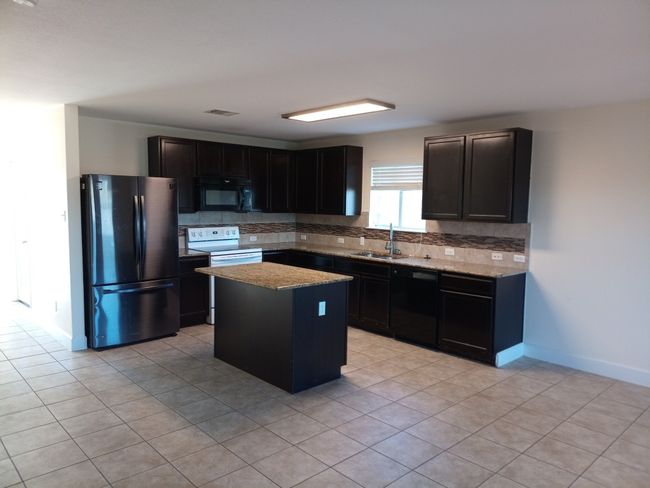 Kitchen featuring black appliances, backsplash, a center island, light tile patterned floors, and dark cabinetry | Image 5