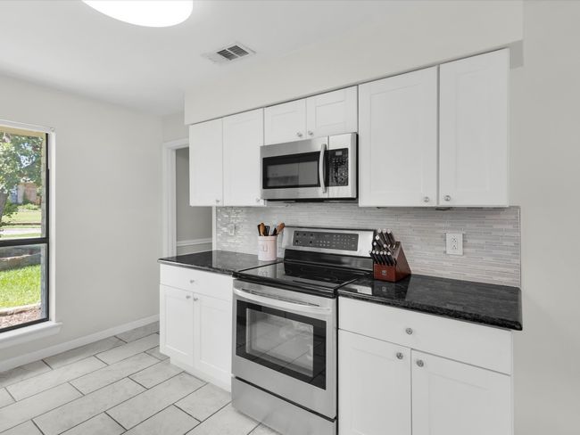 Kitchen with stainless steel appliances, tasteful backsplash, white cabinetry, and dark stone countertops | Image 6