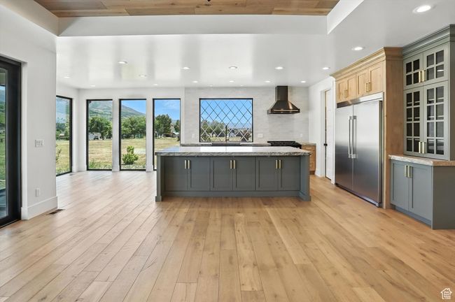 Kitchen with stainless steel built in refrigerator, wall chimney range hood, gray cabinets, light wood-style flooring, and recessed lighting | Image 5