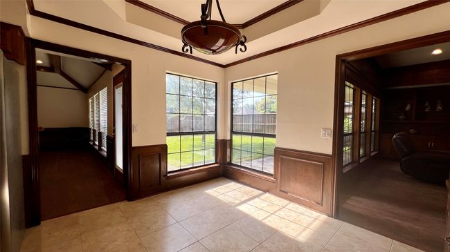 Doorway to outside with wainscoting, ornamental molding, light tile patterned floors, a tray ceiling, and lofted ceiling | Image 8