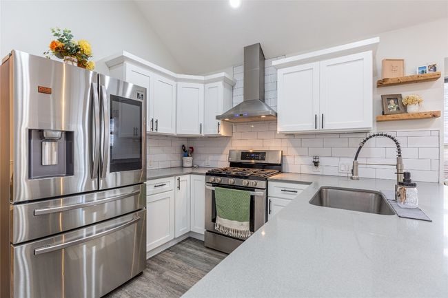 Kitchen featuring stainless steel appliances, wall chimney range hood, a sink, white cabinetry, and lofted ceiling | Image 12