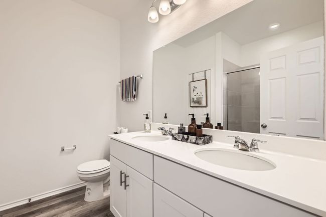 Bathroom with double vanity, tiled shower, toilet, and wood finished floors | Image 17