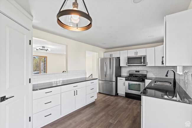 Kitchen featuring dark wood finished floors, white cabinetry, a sink, and appliances with stainless steel finishes | Image 7