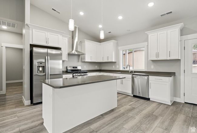 Kitchen featuring stainless steel appliances, wall chimney exhaust hood, a sink, dark countertops, and white cabinetry | Image 14