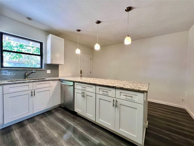 Kitchen with stainless steel dishwasher, a sink, a peninsula, white cabinetry, and dark wood-style flooring | Image 7