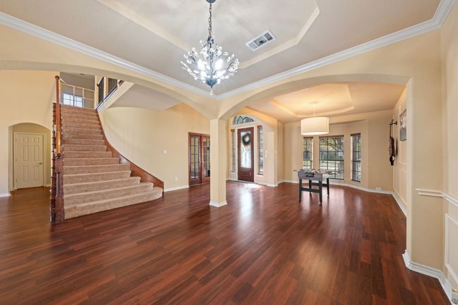 Foyer with dark wood-style floors, stairs, visible vents, a tray ceiling, and arched walkways | Image 12