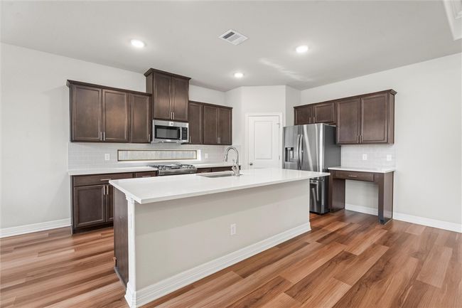 Kitchen with stainless steel appliances, a sink, backsplash, dark brown cabinetry, and light wood-type flooring | Image 11