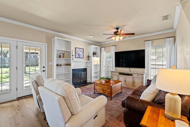 Living area featuring a ceiling fan, wood finished floors, visible vents, a fireplace with flush hearth, and crown molding | Image 5