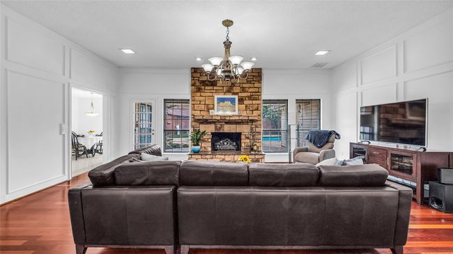Living area featuring a stone fireplace, a chandelier, wood finished floors, healthy amount of natural light, and a decorative wall | Image 21