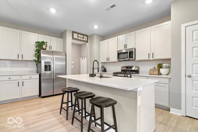 kitchen featuring stainless steel appliances, light wood-type flooring, decorative backsplash, a kitchen bar, and a kitchen island with sink | Image 12