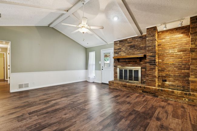 Unfurnished living room featuring a brick fireplace, dark wood finished floors, a ceiling fan, a textured ceiling, and wainscoting | Image 8