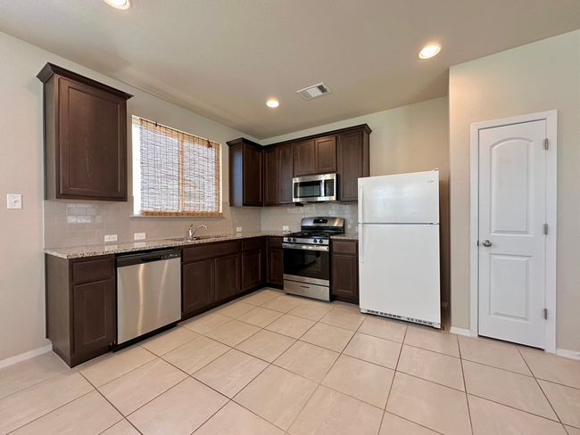 Kitchen with stainless steel appliances, dark brown cabinets, tasteful backsplash, light stone counters, and light tile patterned flooring | Image 9