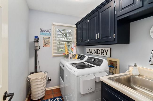 Clothes washing area with dark tile patterned flooring, sink, washing machine and dryer, and cabinets | Image 22