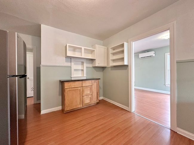 Kitchen with freestanding refrigerator, a wall mounted AC, light wood-style floors, open shelves, and dark countertops | Image 22