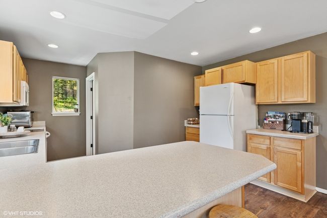 Kitchen with white appliances, light brown cabinetry, a peninsula, recessed lighting, and light countertops | Image 9